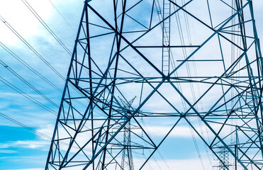 Fototapeta premium High voltage electricity transmission towers with steel lattice structure support power grid infrastructure against blue sky for energy distribution, engineering and utility network. Electrical grid.