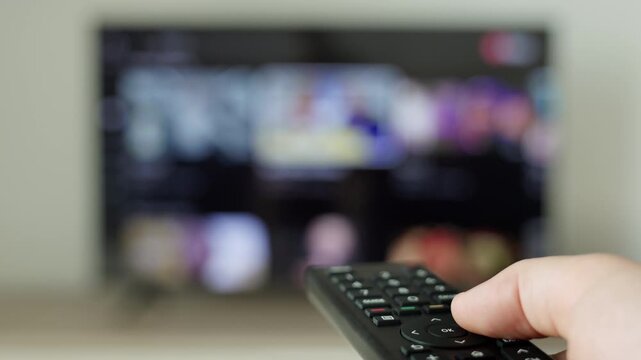 Close-up of a person using TV remote control to browse streaming platforms on a smart television. Concept of home entertainment, digital media, online content, binge watching, and streaming technology