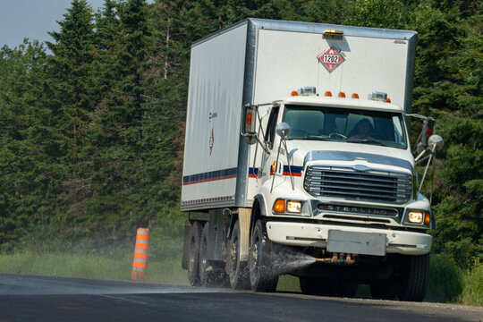 Quebec, Canada, 29 June 2026 : A white Sterling commercial truck drives on a wet road, spraying water, with a hazardous materials placard visible.