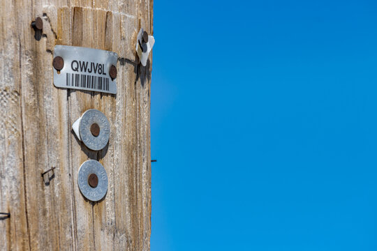 Quebec, Canada, 26 April 2026 : A wooden utility pole features a metal identification tag with a barcode and alphanumeric code.