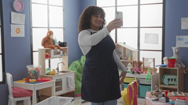 Woman teacher points smartphone for selfie while holding stuffed toy in building; connection warmth.
