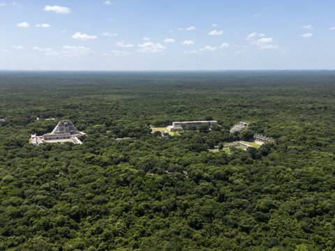 Aerial view of the ancient Mayan archaeological site of Uxmal surrounded by dense jungle canopy under a clear blue sky in Uxmal, Yucatan, Mexico.