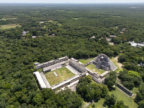 Aerial view of the ancient Mayan ruins of Uxmal, featuring the Pyramid of the Magician and the Nunnery Quadrangle set amidst the lush green jungle canopy in Uxmal, Yucatan, Mexico.