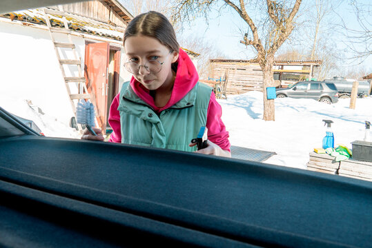 Girl cleaning a car in a snowy yard during winter at a house