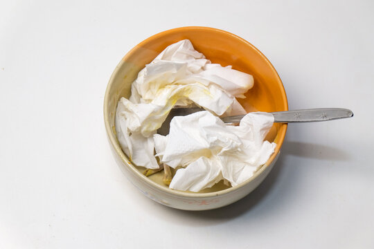 ceramic bowl filled with crumpled used white paper tissues and a metal spoon resting inside.