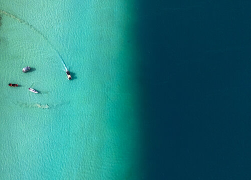 Aerial view of Bacalar lagoon showing the striking contrast between turquoise shallow waters and deep blue depths with small boats navigating the surface in Bacalar, Quintana Roo, Mexico.