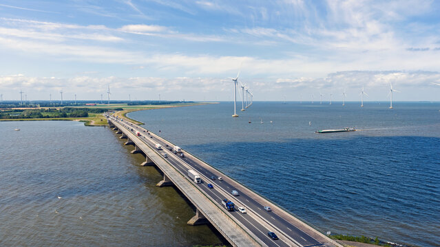 Aerial view of Ketelbrug bridge spanning the water with traffic, accompanied by a line of offshore wind turbines and a barge in the distance, Swifterbant, Flevoland, Netherlands.