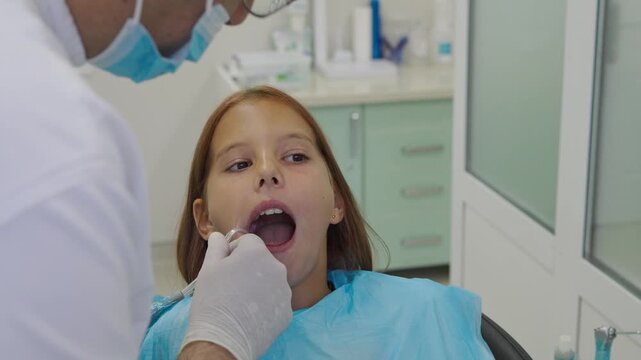 Pediatric dentist inserting saliva ejector for young girl during treatment.