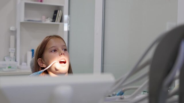 Pediatric dentist inserting saliva ejector for young girl during treatment.