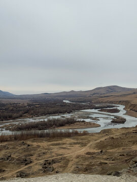 Winding river cutting through dry valley landscape with distant hills.