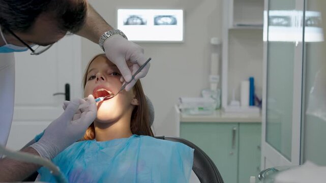 Pediatric dentist giving local anesthesia injection to young girl patient.