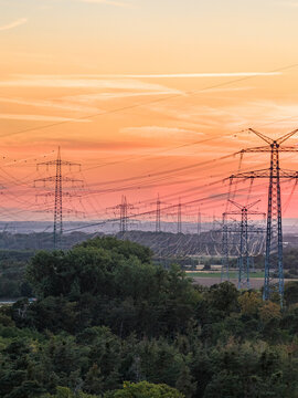 Aerial view of the Amprion-Umspannwerk power lines at sunset, with high-voltage pylons stretching across the landscape above dense trees in Pfungstadt, Hessen, Germany.
