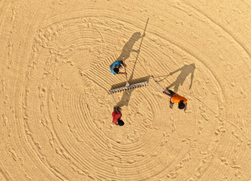 Aerial view of workers raking harvested rice grains into circular patterns on a large drying yard in Ashuganj, Chittagong Division, Bangladesh.