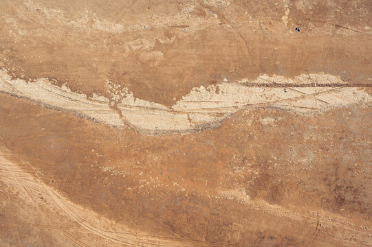 Aerial view of the arid desert landscape of Socotra, featuring textured sand, rocky terrain, and faint vehicle tracks across the barren ground in Socotra, Yemen.