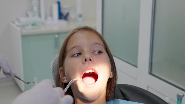 Pediatric dentist examining teeth with mirror for young girl close up.