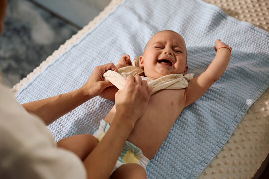 Baby boy crying while mother is changing his clothes at home.