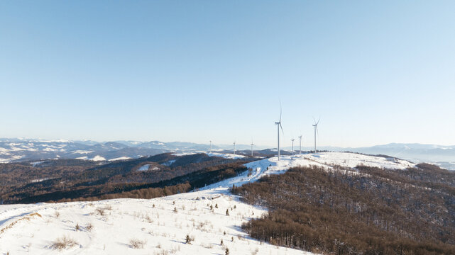 Wind turbines stand tall on a snow-covered mountain landscape under a clear sky