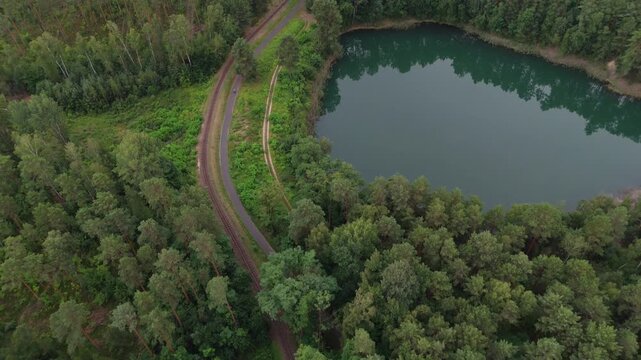 Small forest lake ringed by trees and a curving track with a Cyclist