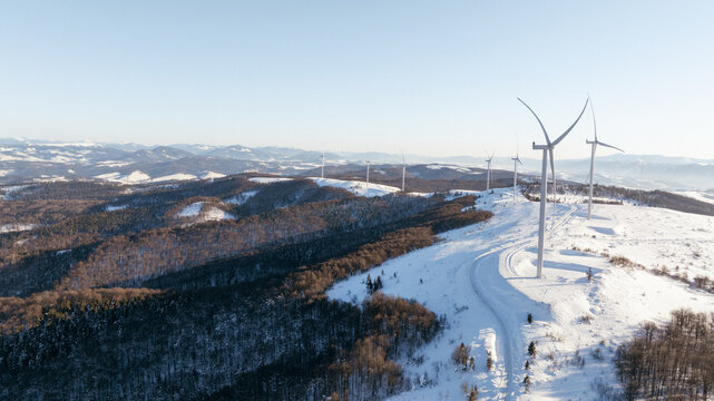 Wind turbines stand tall on a snow-covered mountain range under a clear sky