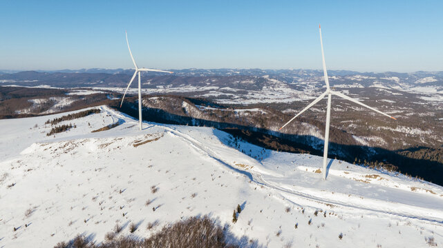 Wind turbines stand tall on a snow-covered mountain landscape under a clear sky