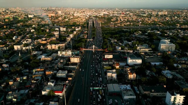 Santo Domingo Este, Dominican Republic - 24 July 2026: Aerial view of the busy bridge and highway traffic flowing through the dense urban landscape at sunset.