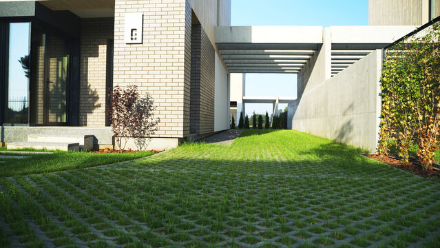 Permeable pavers driveway with green grass leading to a contemporary residential facade and concrete walls