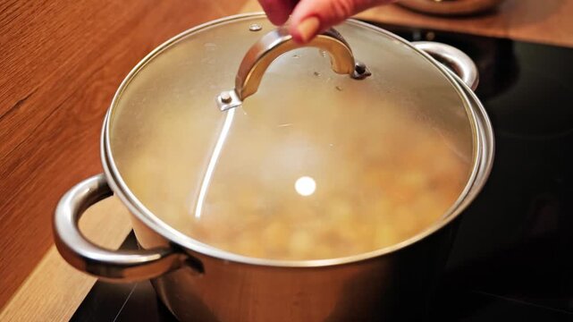 Steam escapes as saucepan lid lifts, reveals simmering broad beans, slow motion