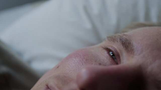 Extreme close up shot of man lying in bed, waking up or struggling to sleep. Ideal for medical commercials about insomnia, sleep aids, mental health apps, or bedding brands
