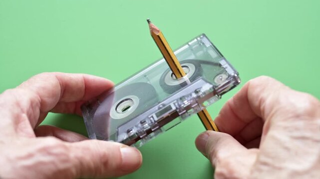 Hands Rewinding Vintage Cassette Tape With Pencil Against Green Background