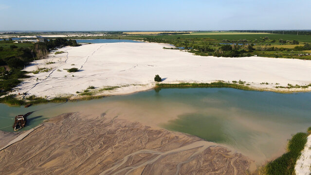 Sand quarry operation showing industrial dredging creating a new sand formation in an artificial lake with surrounding fields