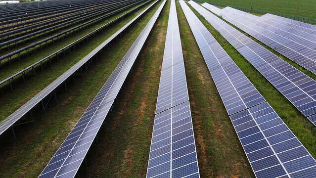 Solar farm generating clean energy with photovoltaic panels across green field, aerial view showing renewable power future