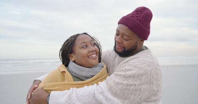 African American couple on beach, man coming from right wrapping woman in yellow shawl keeping warm