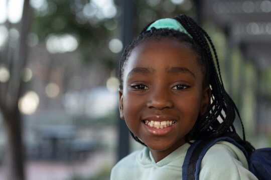 African youth female smiling and looking at camera at park, wearing mint hoodie and backpack