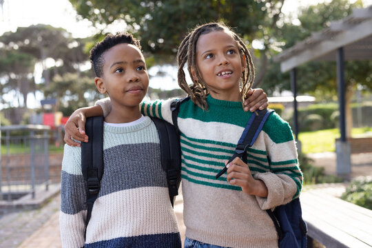African American preteen boys walking on paved school path carrying backpacks in striped sweaters