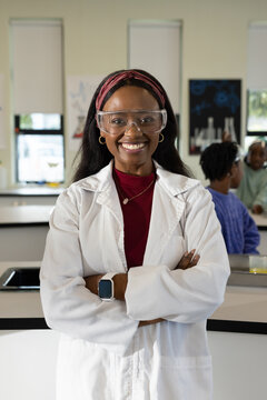 African American female teacher wearing lab coat, goggles, supervising youth females at lab benches