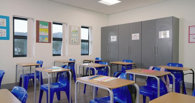 Camera is panning across classroom to reveal desks, chairs, backpacks, posters, cabinets