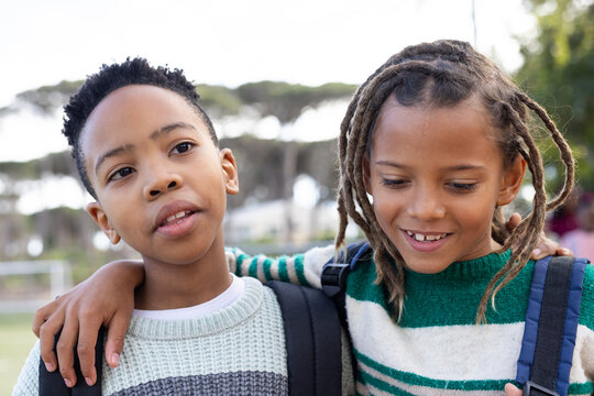 Two African American teenage boys posing arm over shoulder on field in striped knits and backpacks