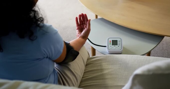 Senior African American woman adjusting cuff tubing on sofa, reaching BP unit on table, copy space