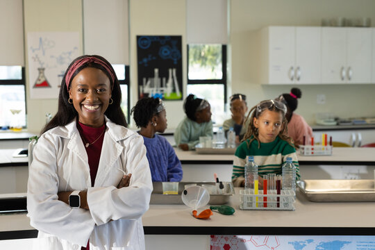 African American teacher wearing lab coat guiding teenage students in school lab with test tubes