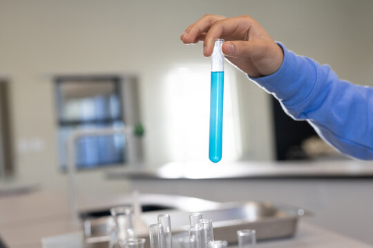 African American teen in light-blue top holding glass test tube filled bright blue liquid at lab