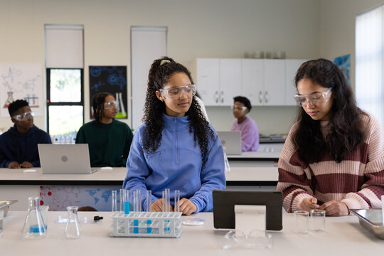 African American teen girls wearing safety goggles doing experiments in school lab with test tubes