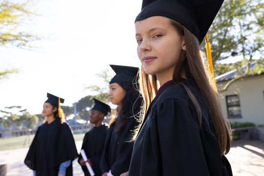 Diverse students on campus wearing gowns caps diploma right youth female facing camera, copy space