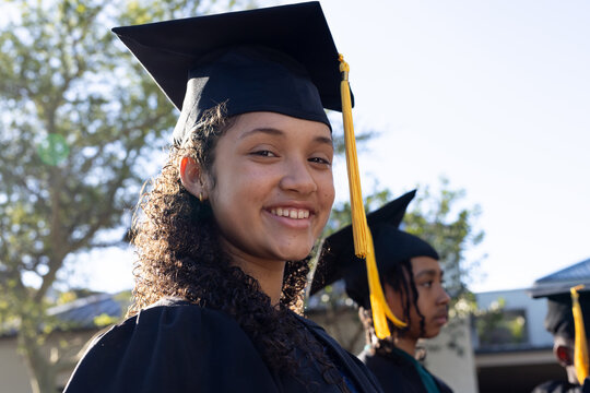 African American graduates smiling on campus wearing black mortarboards, yellow tassels, gowns