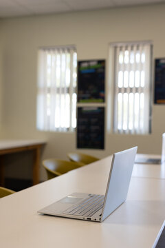 Silver laptop is sitting open on long white table in study room, with mustard chairs