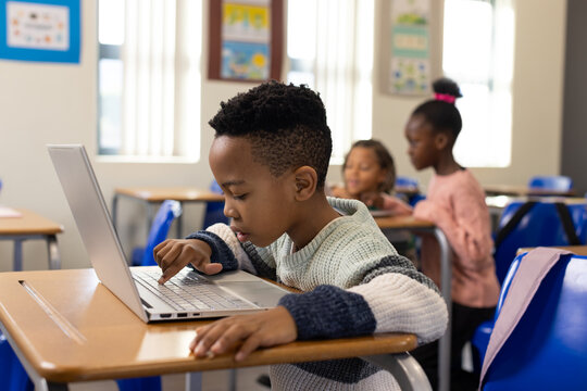 African American children with boy in striped sweater working on silver laptop at classroom desk