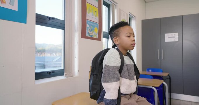 Preteen boy responding to camera, smiling and speaking in classroom with backpack, wearing sweater