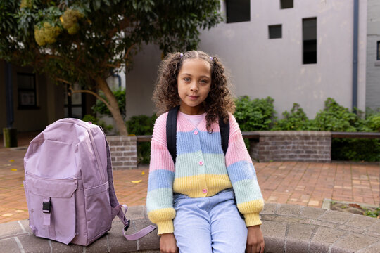 African American youth sitting on ledge in quad wearing cardigan lavender-backpack black-straps
