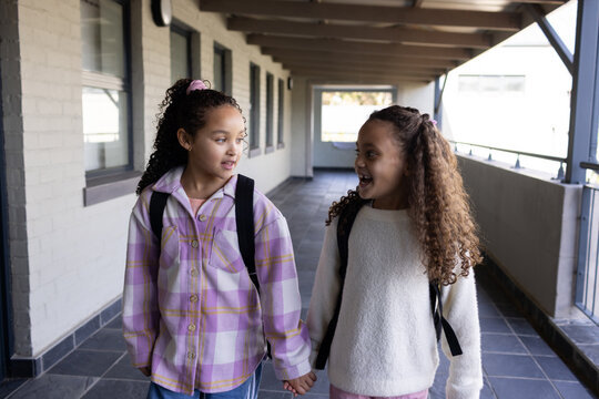 African American teenage female students walking holding hands down school corridor with backpacks