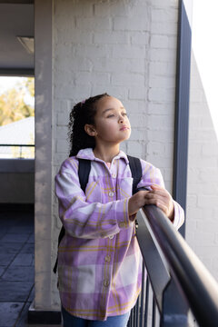 African American teen girl standing on walkway leaning on railing with plaid overshirt backpack
