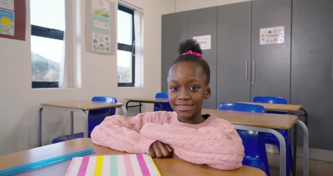 African child turning and smiling at desk while camera approaching, striped notebook, blue ruler